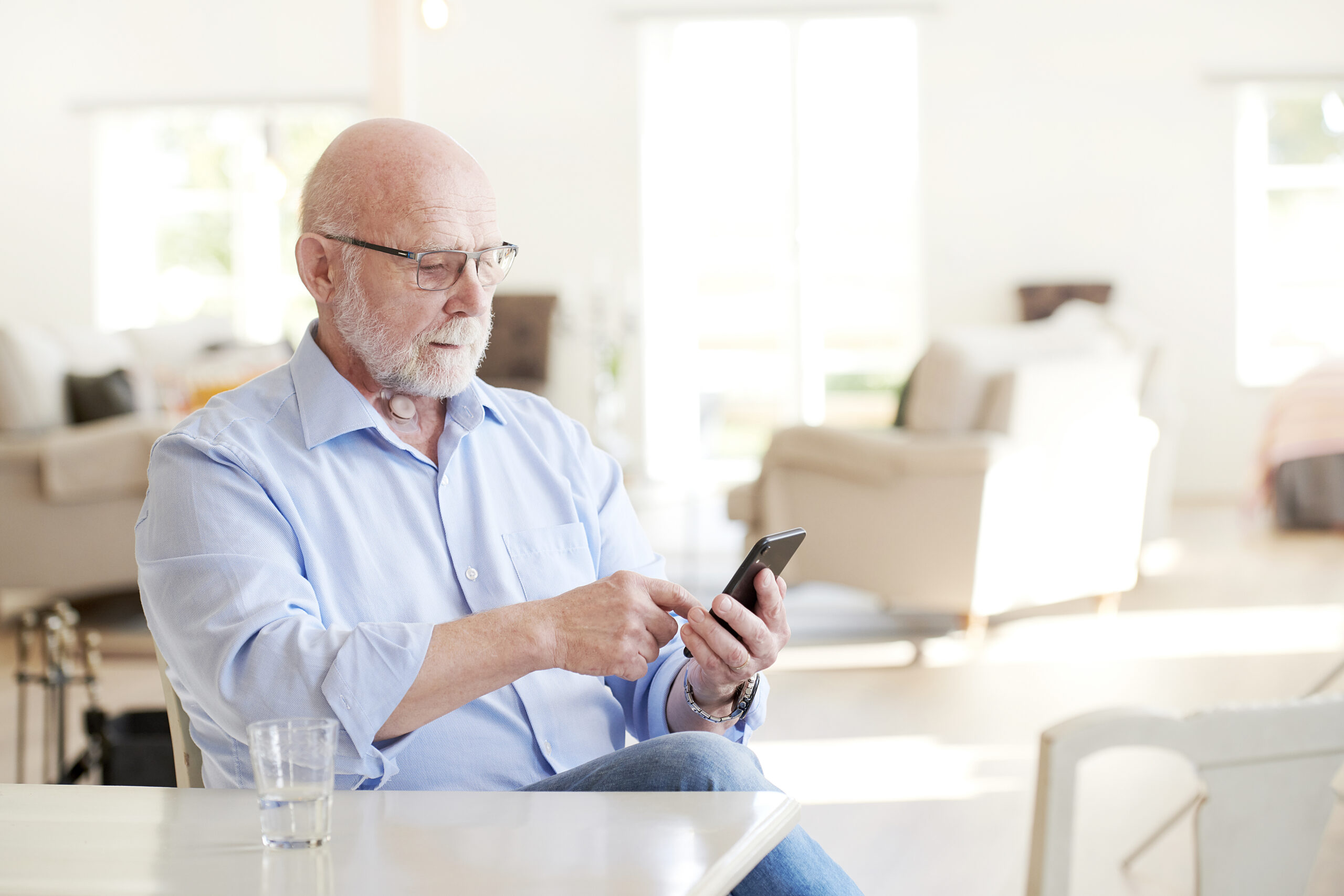 Image of man sat at the kitchen table looking down at his mobile phone.