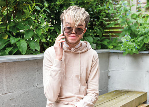 Man sat on a bench outside, talking to someone on his mobile phone.