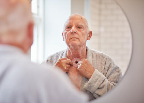 Man looking in the mirror at this stoma whilst putting on an adhesive.