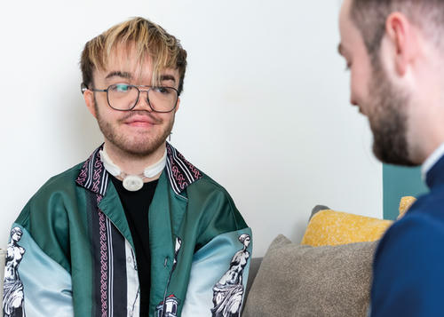 A man is sat on the sofa looking at the male nurse on the right.