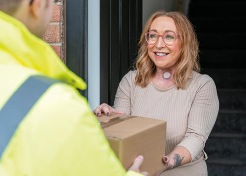 Lady is stood smiling at the door whilst she received her parcel from the delivery man.