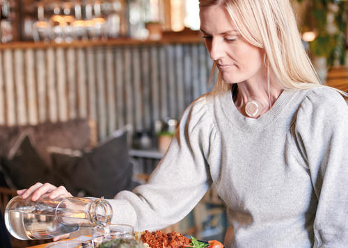 Lady in grey jumper is sat pouring some water into her glass before she has her lunch.