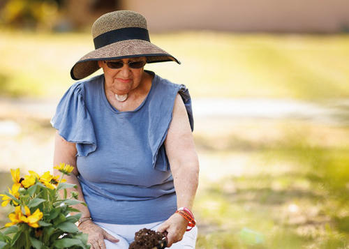 Lady in her garden, gardening, wearing a hat and sunglasses.