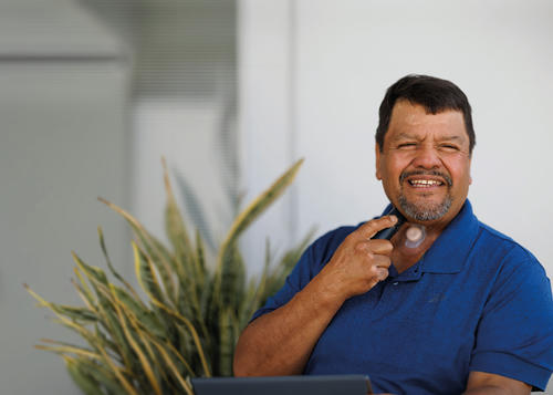 Man wearing a blue polo top, sat smiling.